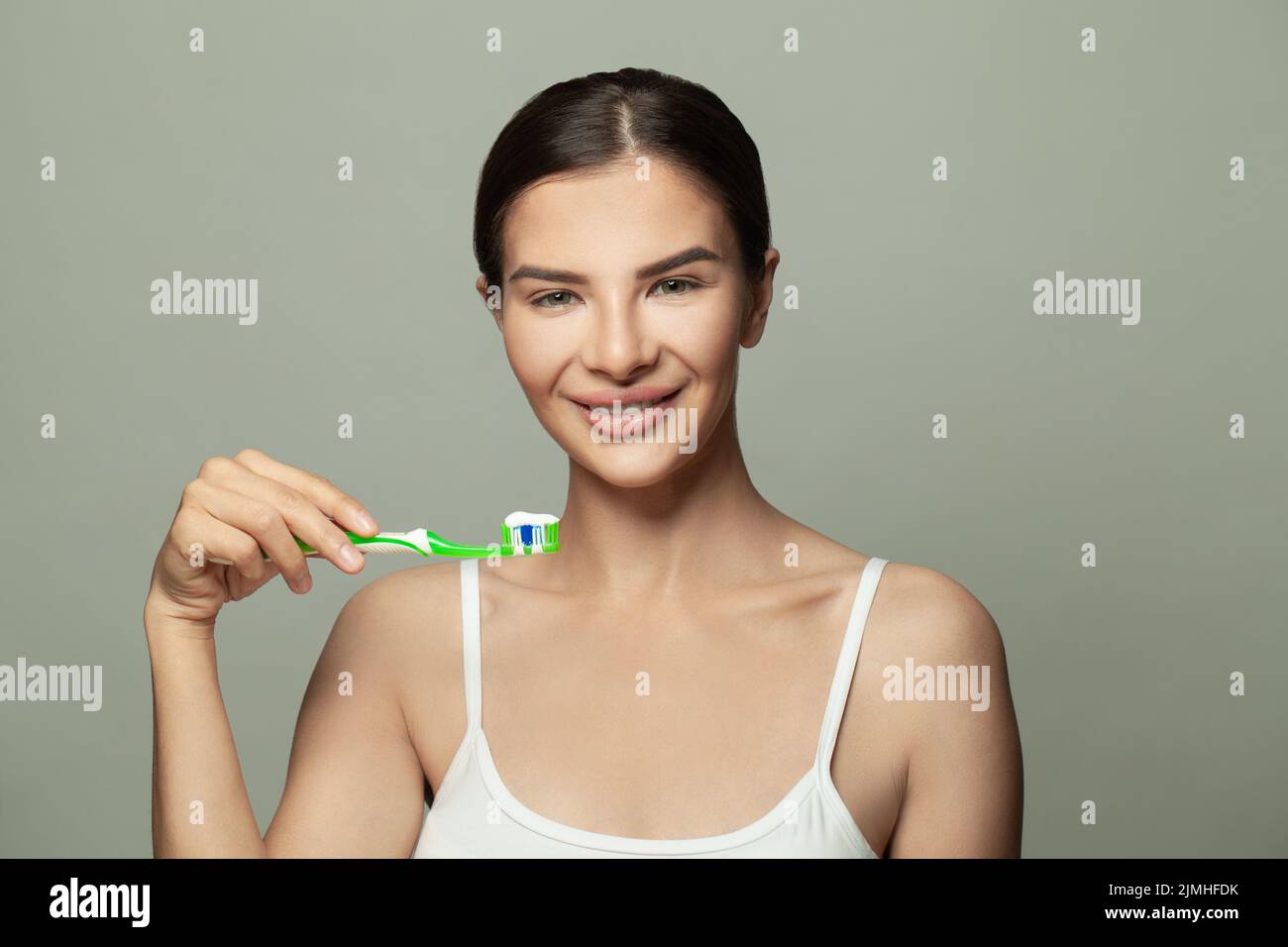 Retrato de belleza de una feliz y bonita mujer morena cepillándose los dientes con un cepillo de dientes y mirando la cámara sobre fondo blanco Foto de stock