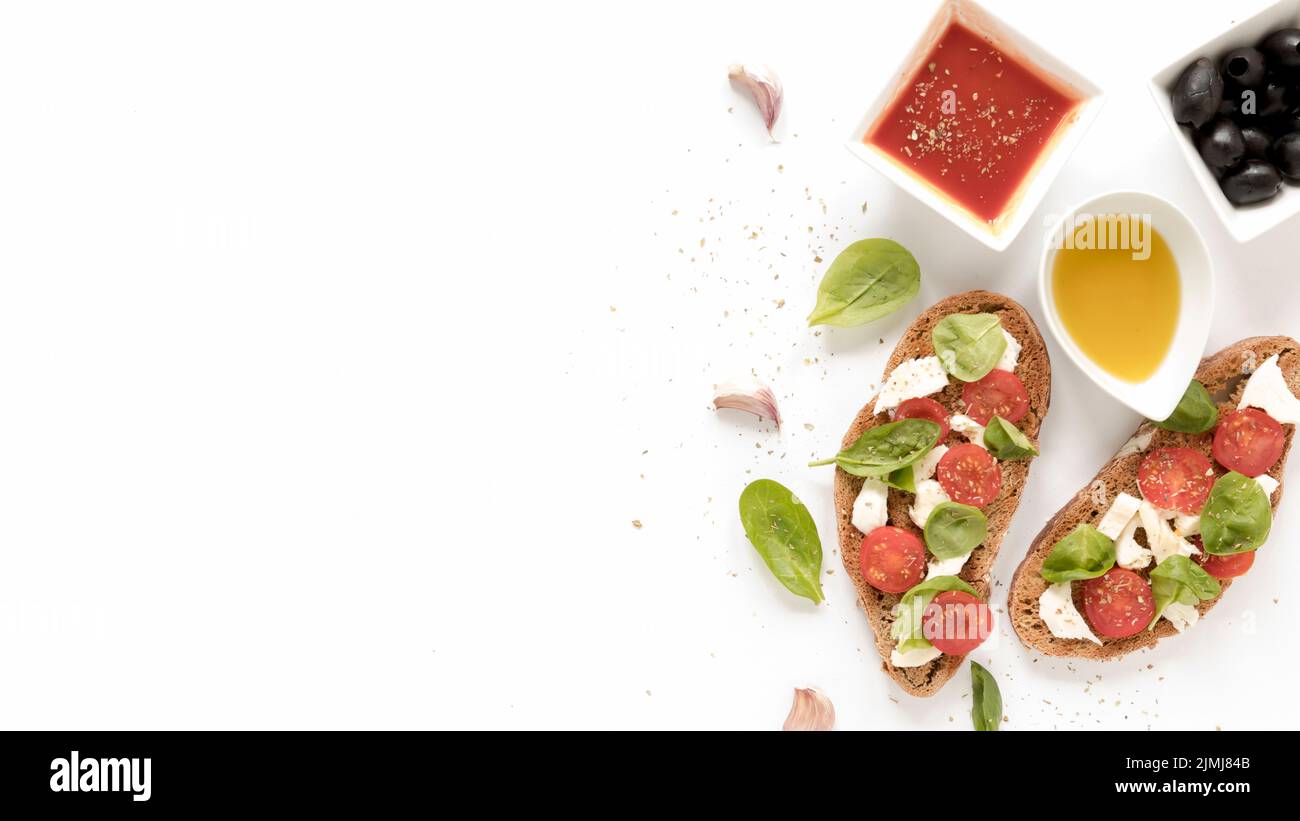 Bruschetta con queso tomate albahaca hojas encima cerca de salsa aceitunas aceite ajo diente blanco superficie Foto de stock