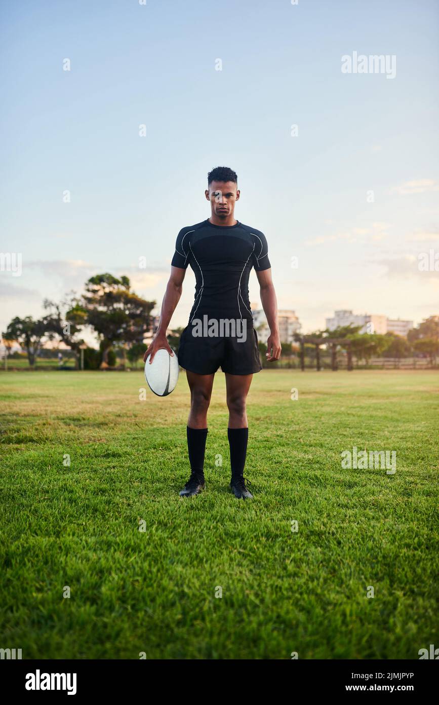 Aplastando mis objetivos deportivos. Retrato completo de un joven deportista de pie y sujetando una pelota de rugby antes de una práctica matutina. Foto de stock