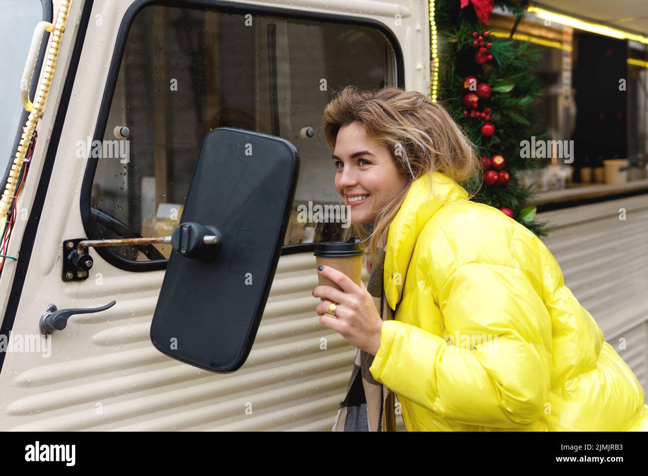 Feliz mujer con una taza de café caliente al lado de la camioneta retro en el mercado de Navidad Foto de stock