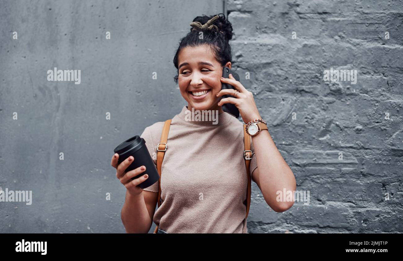 ¿Dónde estás? Una atractiva adolescente de pie sola y utilizando su móvil mientras sostiene una taza de café. Foto de stock