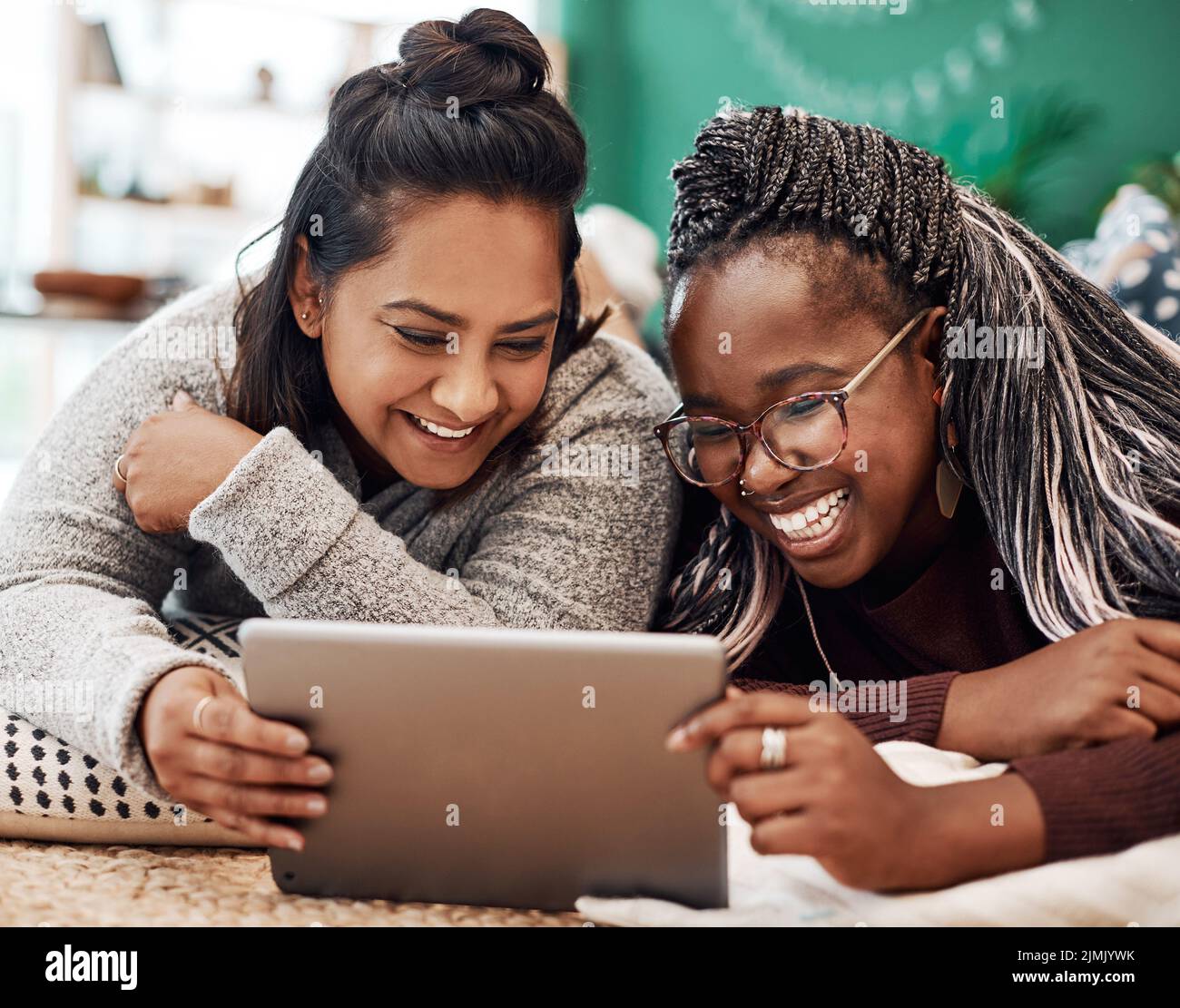 Pase su tiempo con las personas que le hacen reír. Dos mujeres jóvenes usando una tableta digital juntas en el suelo en casa. Foto de stock