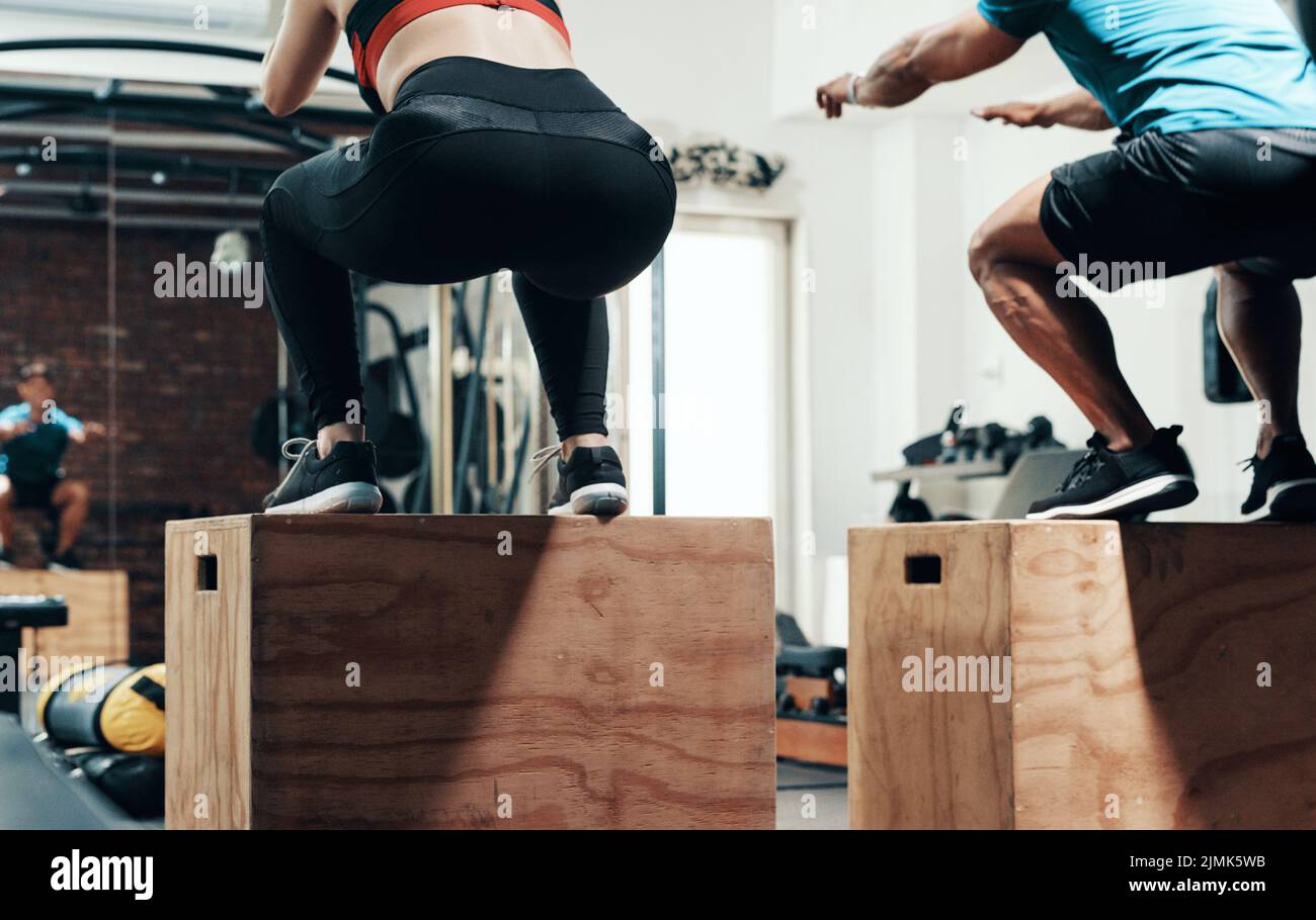 Cuando el estado físico dice saltar, hacer. Dos deportistas irreconocibles saltan en la caja mientras se entrena en un gimnasio. Foto de stock
