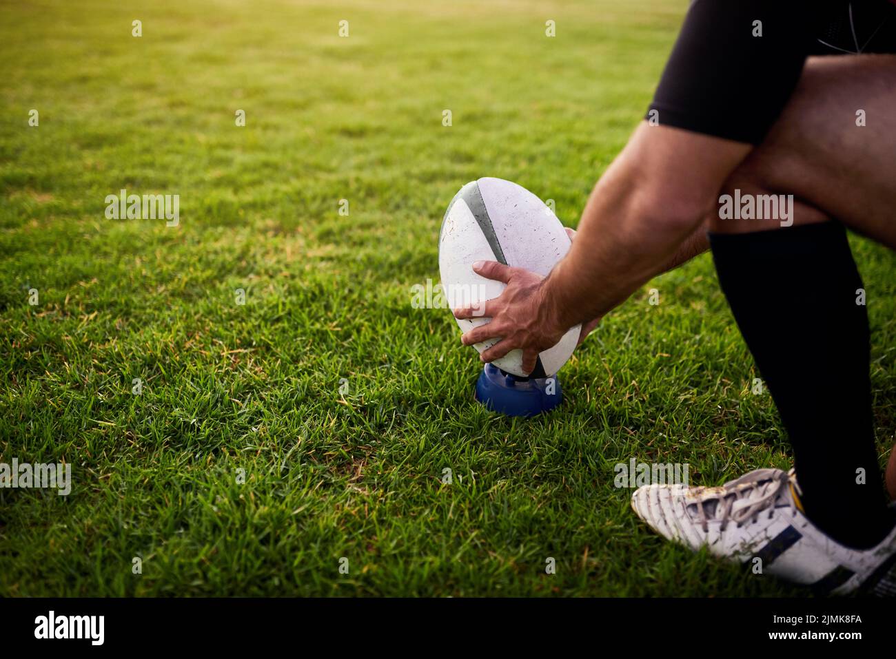 Trabajando en mi habilidad. Un deportista irreconocible agachándose solo durante la práctica de rugby en un club deportivo. Foto de stock