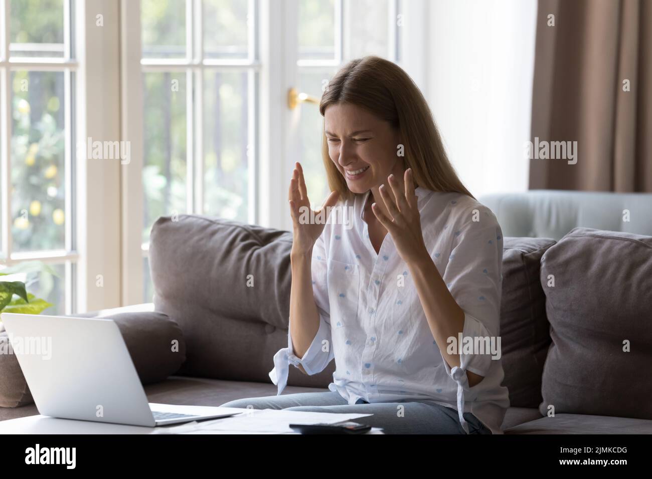 Mujer enojada y nerviosa sentada en la mesa con el ordenador portátil y las cuentas Foto de stock