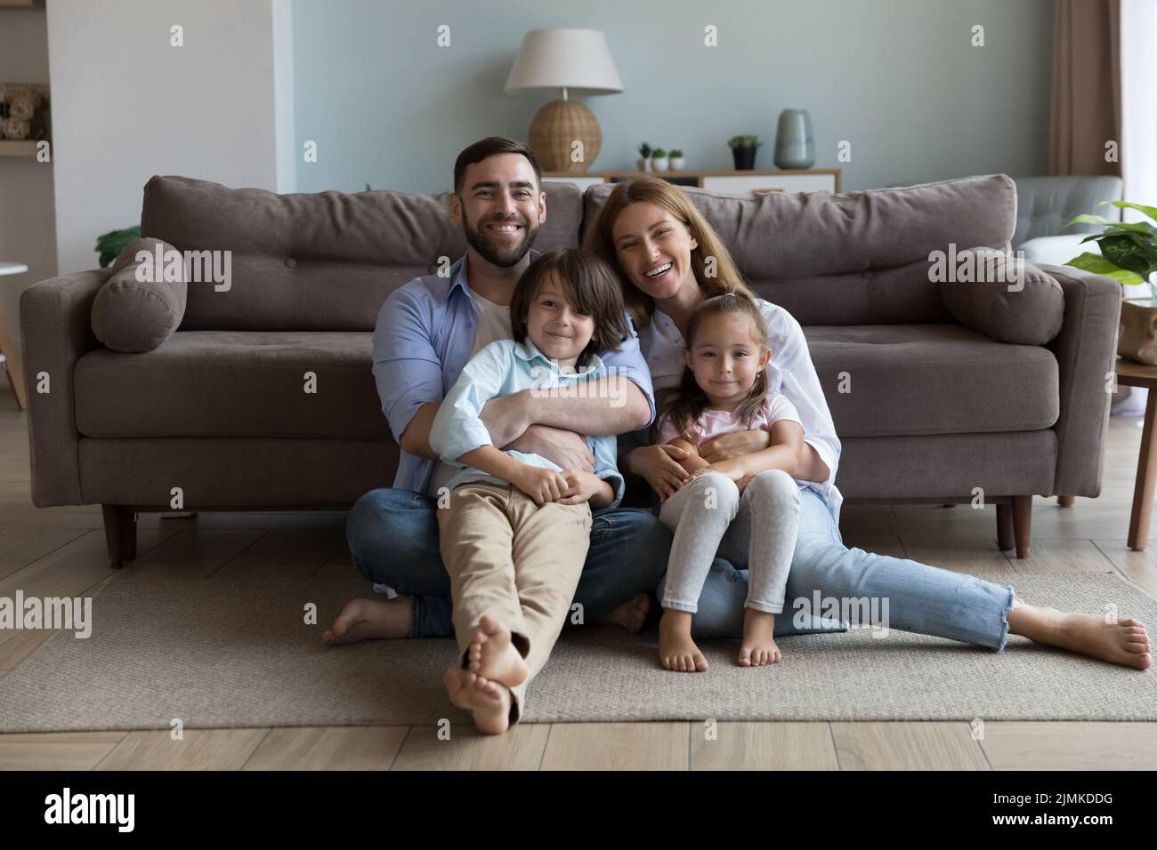 Una pareja con niños pequeños abrazándose se sienta en el piso en casa Foto de stock