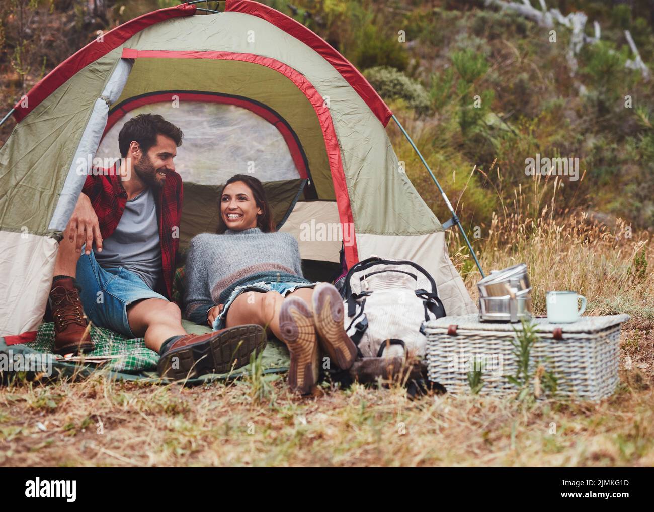 Feliz pareja joven sentada en una tienda de campaña. Pareja alegre disfrutando de sus vacaciones en un camping. Foto de stock