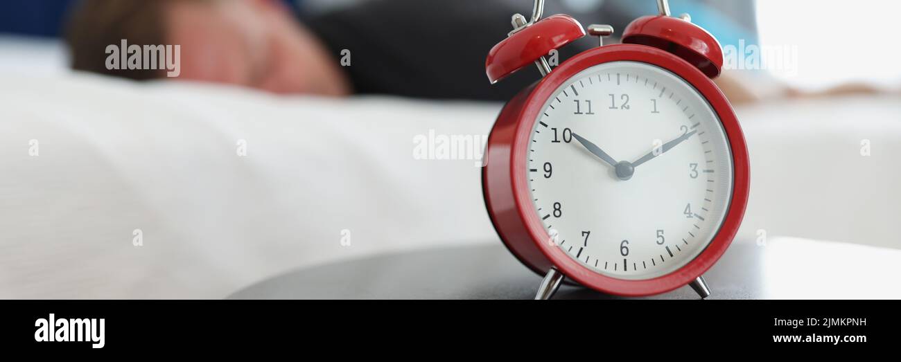 Un reloj despertador rojo está sobre la mesa en el dormitorio Foto de stock