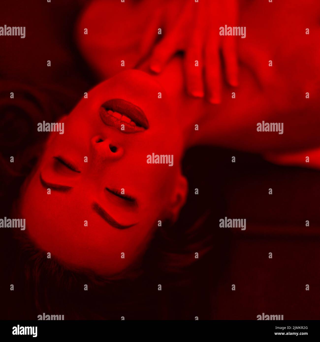 Mujer apasionada tumbada en un sofá con los ojos cerrados en un retrato de luz roja Foto de stock