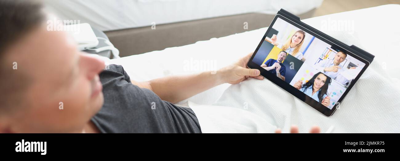 Un hombre en una cama de hotel con una tableta habla a través de un enlace de vídeo Foto de stock