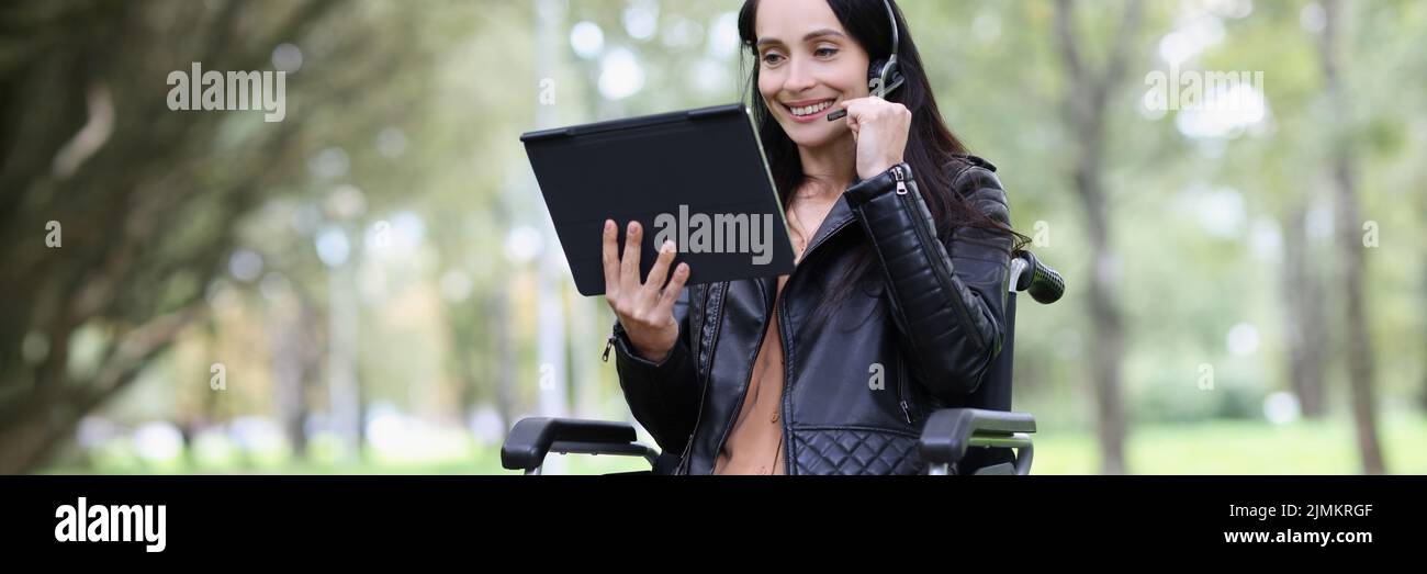 Una mujer joven en silla de ruedas con un auricular y un ordenador portátil Foto de stock