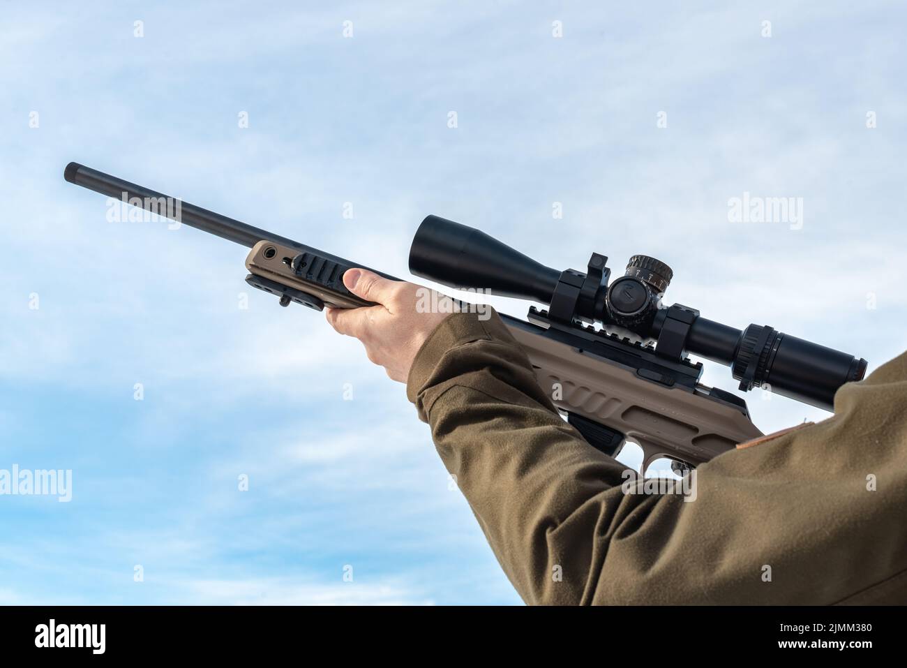 Un rifle de francotirador apunta desde un rifle con una vista óptica en las manos del hombre soleado cielo azul Foto de stock
