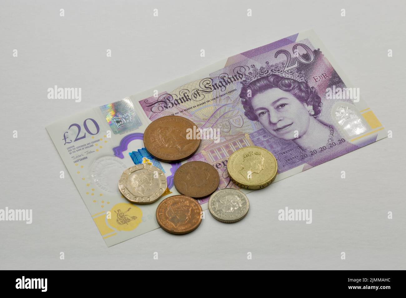 Billete de banco británico de veinte libras esterlinas y primer plano de monedas en blanco. Retrato de la reina Isabel II. Foto de stock