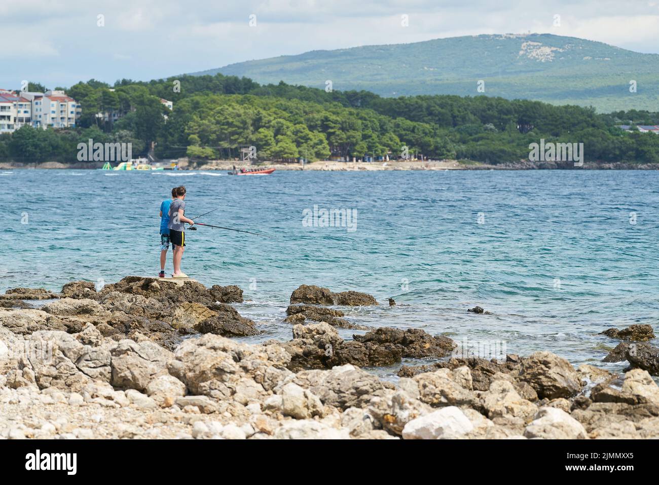 Dos niños de pie en la costa rocosa cerca de la ciudad de Krk en Croacia pescando Foto de stock