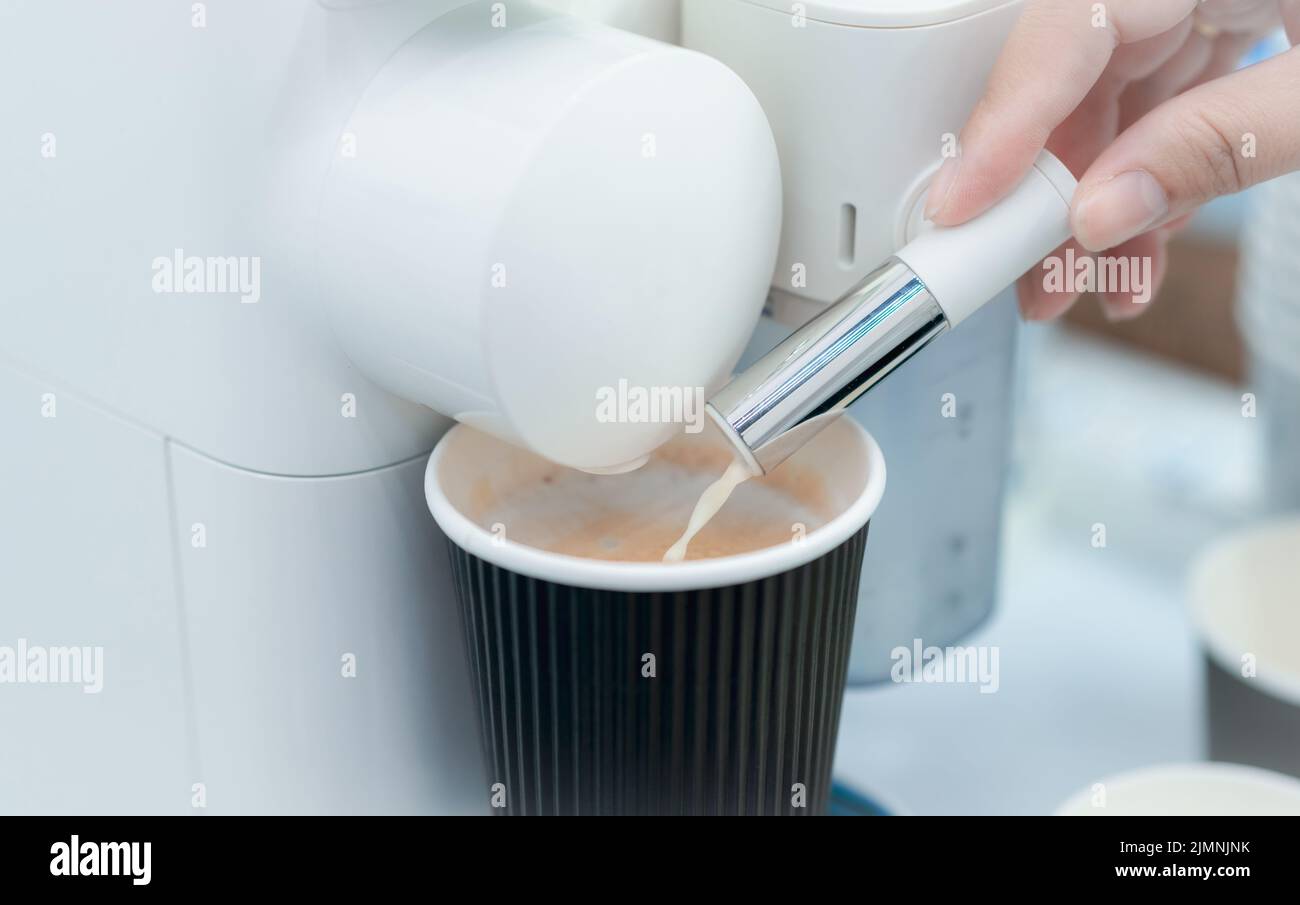 Mujer haciendo una taza de café caliente con cafetera cápsula. Mujer mano sosteniendo el dispensador de espuma de leche de la cafetera de cápsula sobre la mesa. Latte Foto de stock