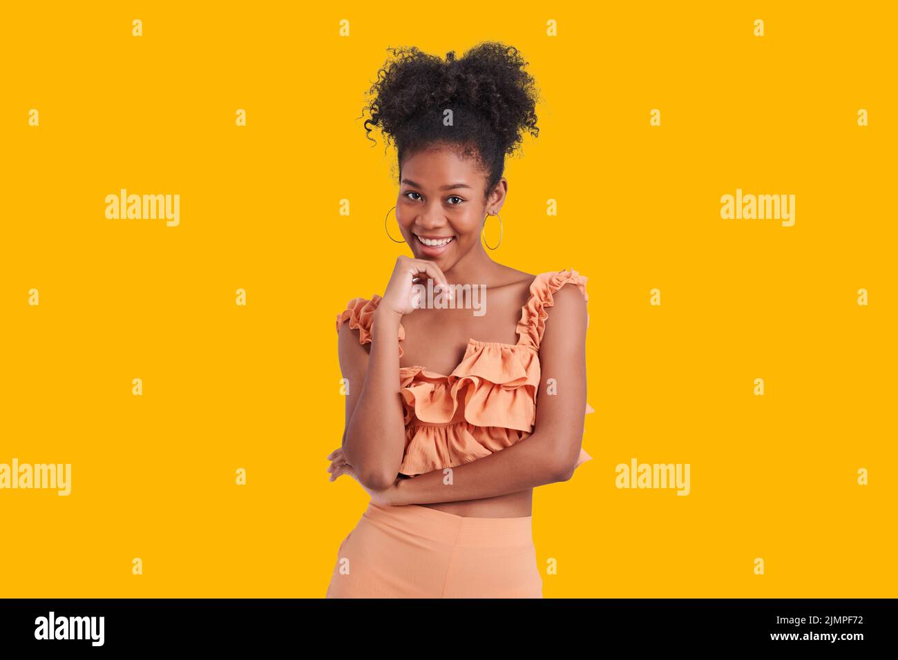 Hermosa niña afroamericana con vestido de camisa naranja desgaste un afro peinado sonriente encantador aislado color amarillo fondo. Foto de stock