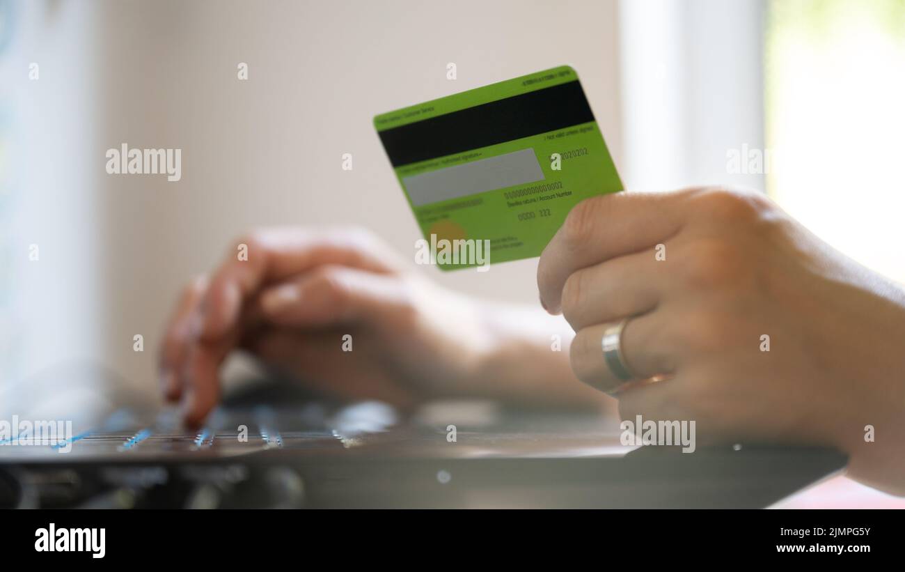 Vista de primer plano de la mano femenina caucásica con tarjeta de crédito mientras navegas por Internet en un ordenador portátil en una imagen conceptual de las compras en línea. Foto de stock