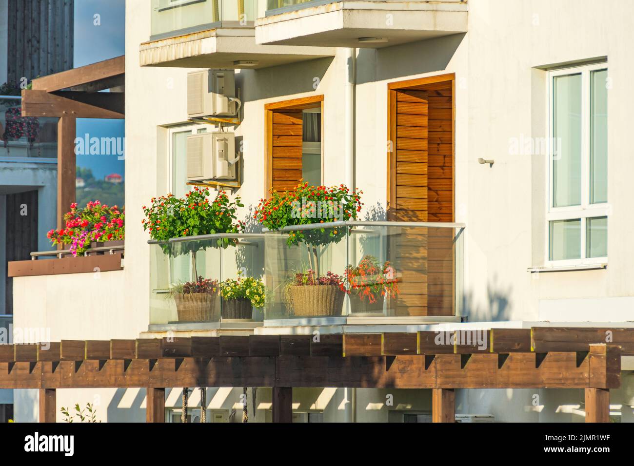 Terraza con plantas y árboles en flor en el balcón iluminado por el sol con elementos de decoración de madera Foto de stock