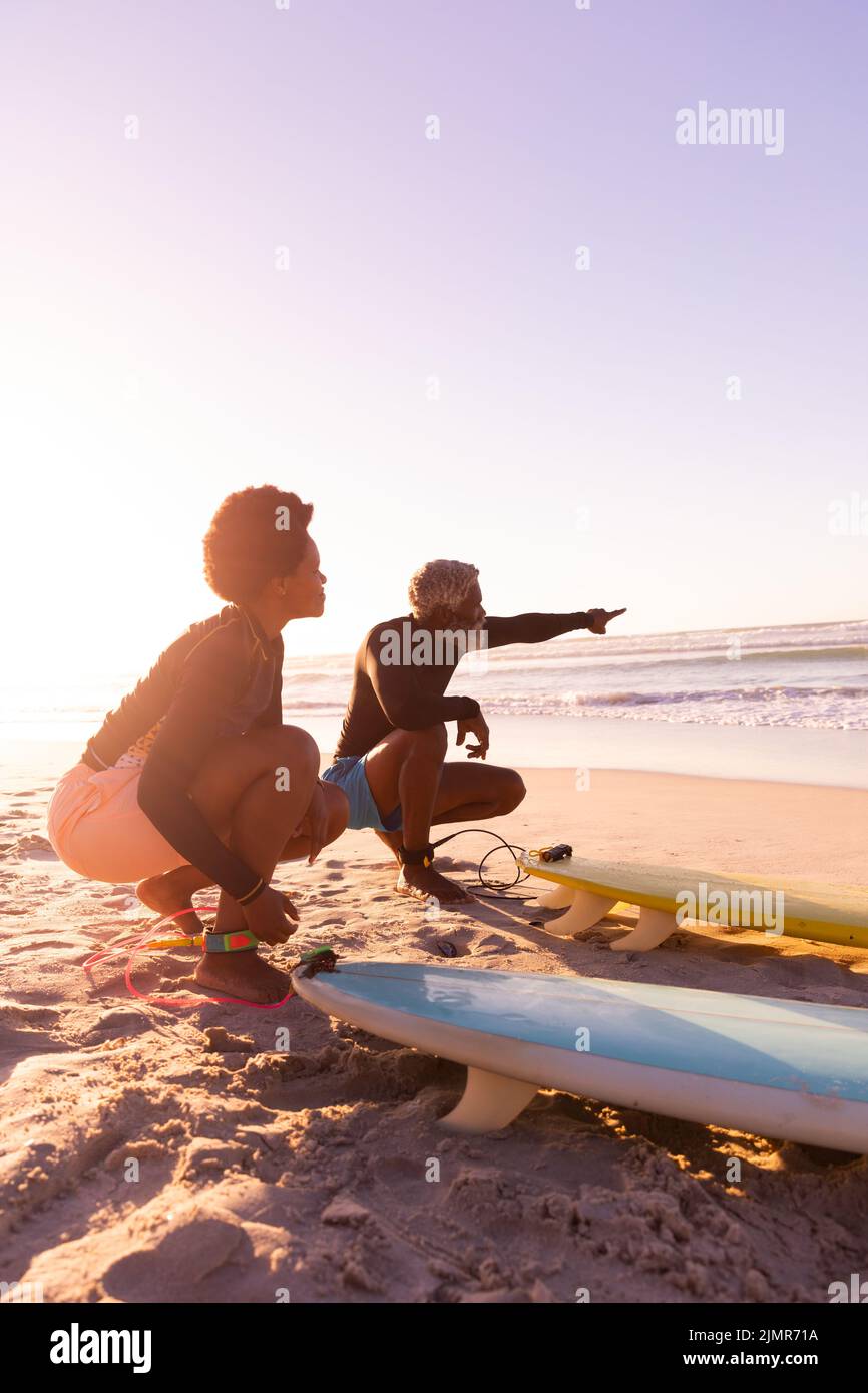 Hombre mayor afroamericano apuntando hacia el mar mientras disfruta con una mujer madura en la playa. Espacio de copia, naturaleza, puesta de sol, inalterado, amor, la unión, Foto de stock