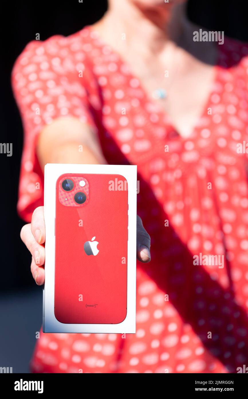 Una mujer, una mujer de mediana edad sosteniendo una nueva caja de iPhone 13 de Apple con su nueva compra de iPhone dentro de la caja. Es un modelo rojo como se muestra en la imagen Foto de stock