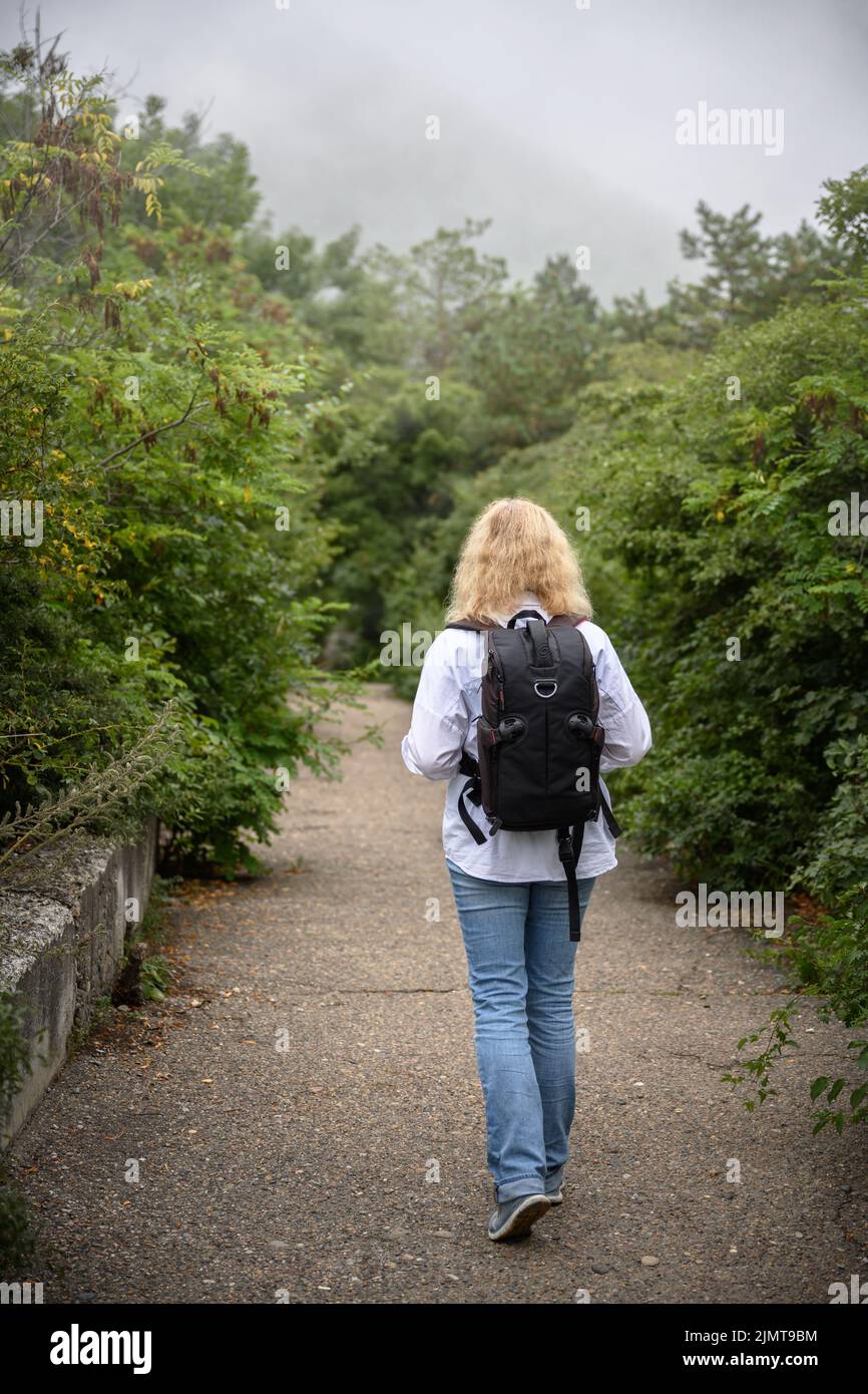 Mujer excursionista solitaria camina en el bosque nublado de la montaña. La chica viajera está sola en el camino en el bosque. La persona joven se va en el sendero del parque. Concepto de caminata, adv Foto de stock