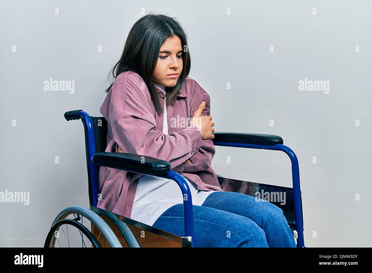 Joven morena sentada en una silla de ruedas temblando y congelada para el  frío de invierno con expresión triste y de choque en la cara Fotografía de  stock - Alamy