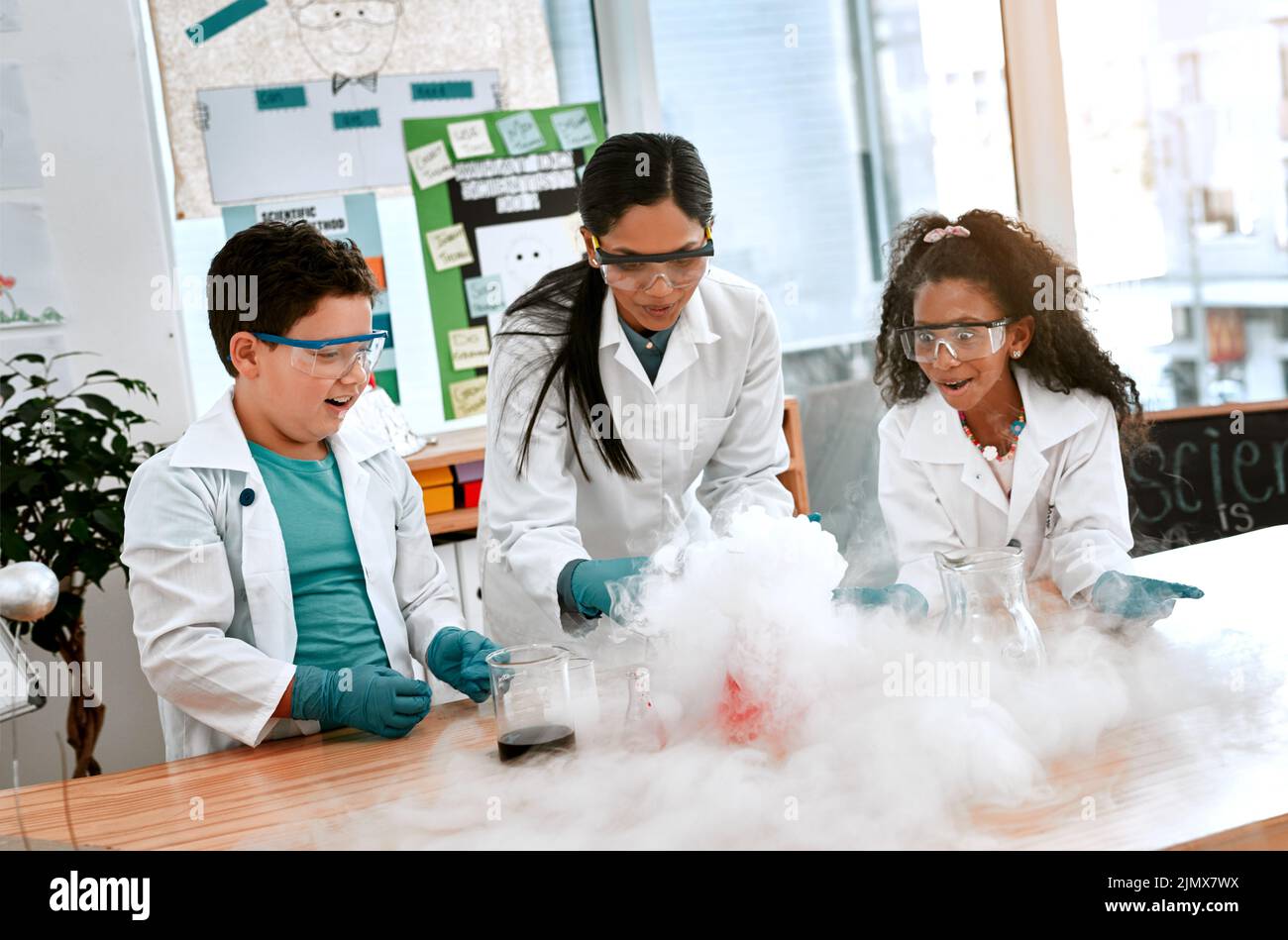 La ciencia pone la moda en la escuela. Un adorable niño y niña realizando un experimento científico con su maestro en la escuela. Foto de stock