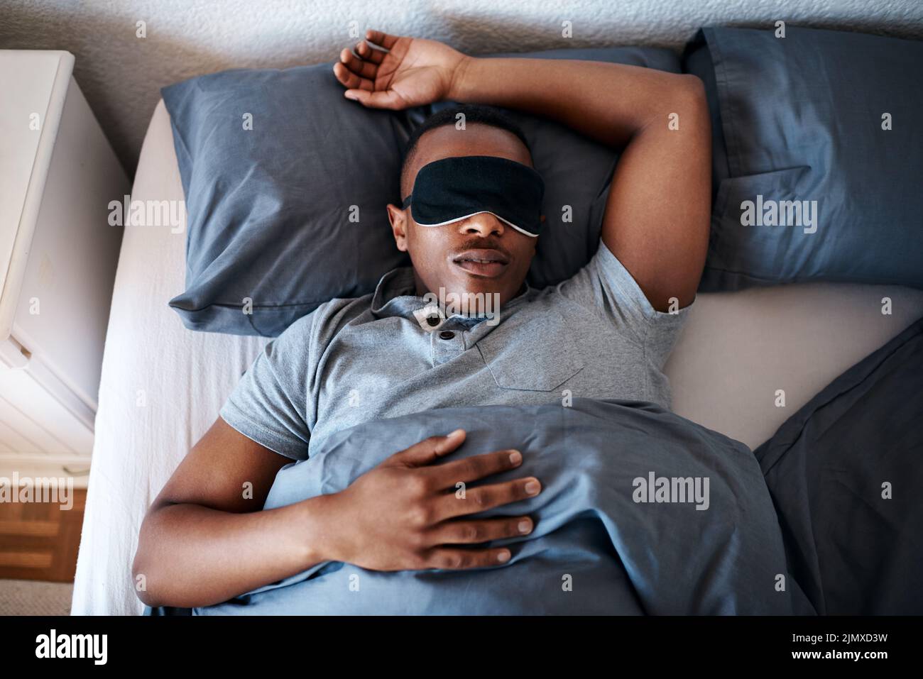 Esto es para lo que son los fines de semana. Un joven guapo usando una máscara de noche y durmiendo en su cama en casa. Foto de stock