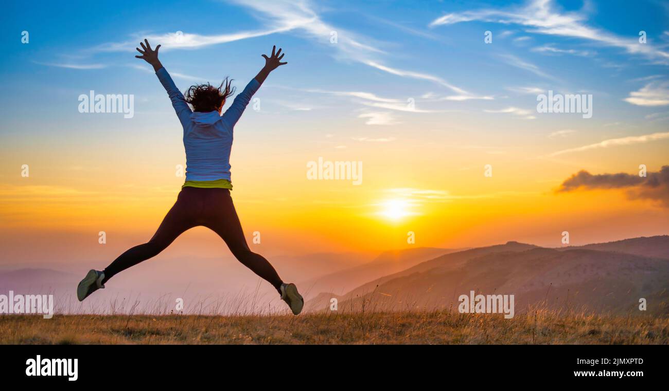 Mujer joven saltando al atardecer en las montañas Foto de stock