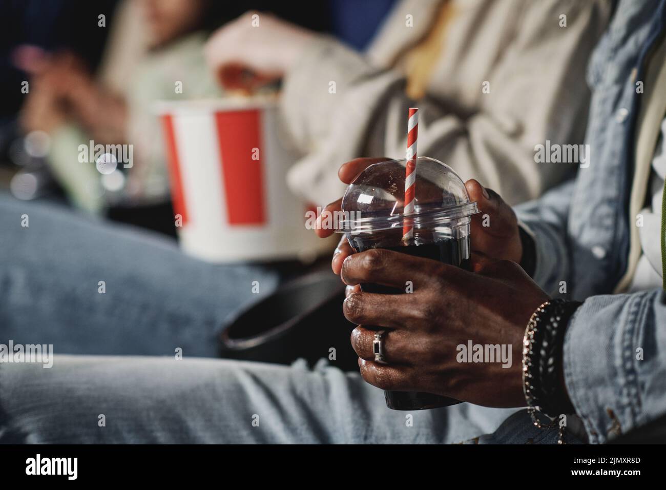 Disparo con enfoque selectivo de un hombre negro irreconocible sosteniendo una taza de plástico con una bebida de cola en el cine Foto de stock