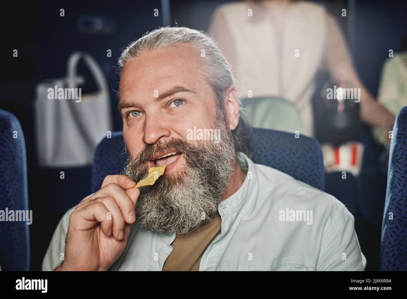 Primer plano de un hombre caucásico maduro con barba en la cara disfrutando de un aperitivo y viendo una película en el cine Foto de stock