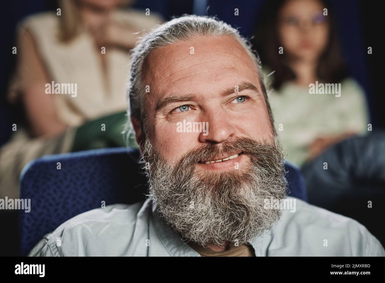 Retrato horizontal de primer plano de un hombre caucásico maduro alegre con barba en la cara viendo una película de comedia en el cine Foto de stock
