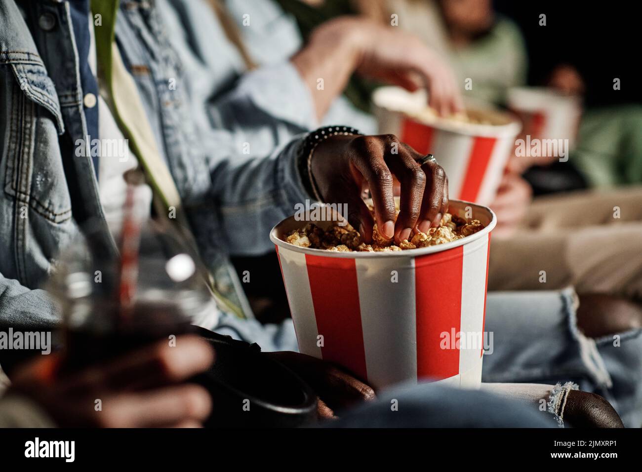 Irreconocible Negro hombre comiendo deliciosas palomitas mientras ve una película en el cine, selectivo enfoque disparo Foto de stock