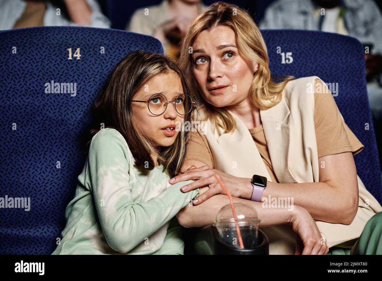 Mujer caucásica y su hija preadolescente sintiéndose asustada al ver una película de terror en el cine Foto de stock