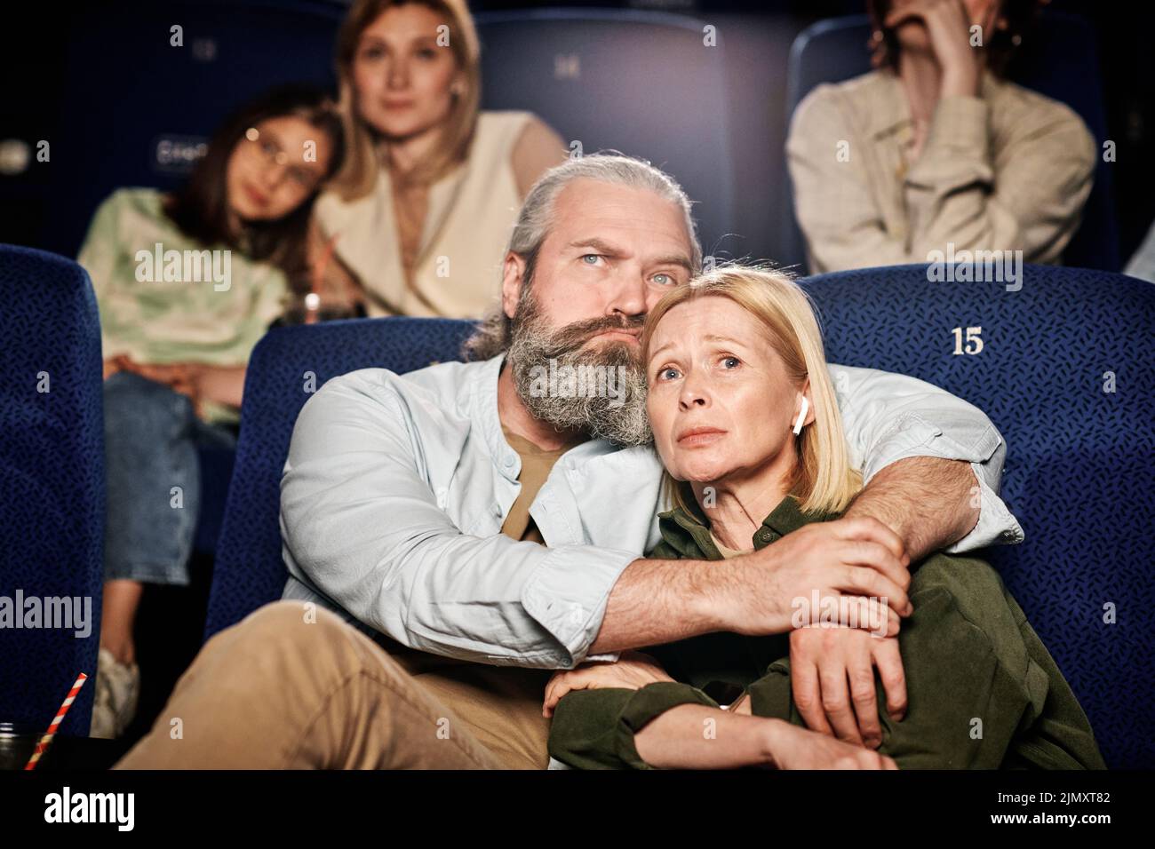 Hombre caucásico adulto con barba en la cara abrazando a su esposa mientras ve una triste película dramática en el cine Foto de stock