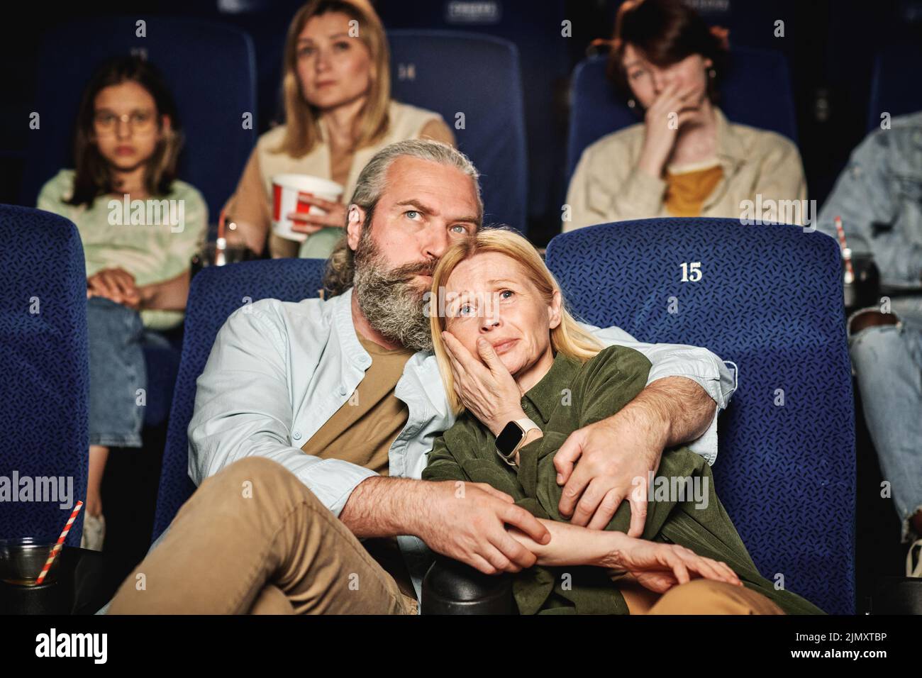 Plano horizontal de un hombre caucásico reconfortante a su esposa mientras ve una película de tragedia en el cine Foto de stock
