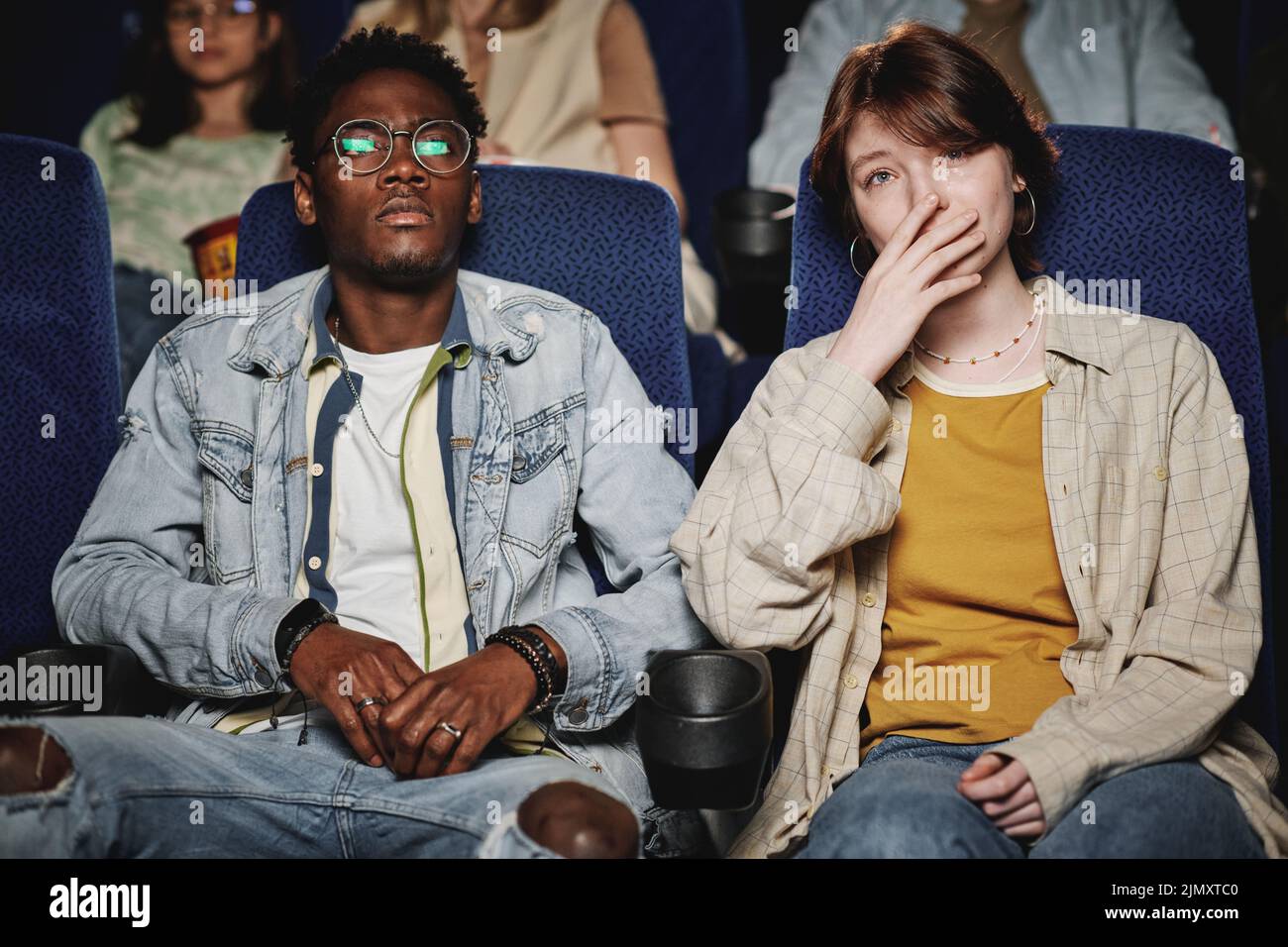 Joven hombre negro y su amiga caucásica viendo una triste película dramática en el cine, joven llorando Foto de stock