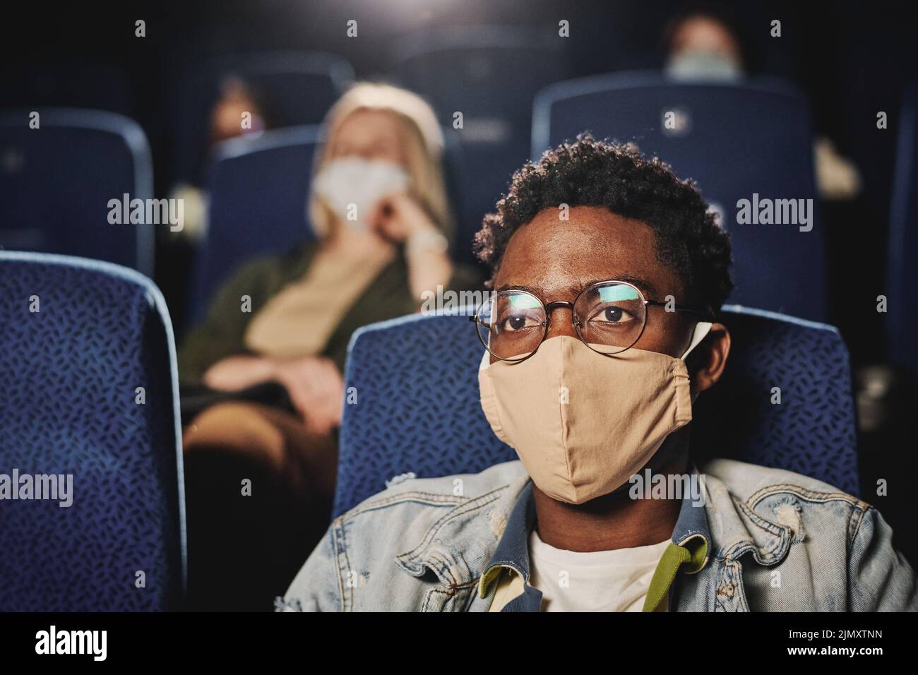Foto de enfoque selectivo de un joven negro con máscara protectora pasando tiempo viendo una película en el cine, concepto de pandemia Foto de stock