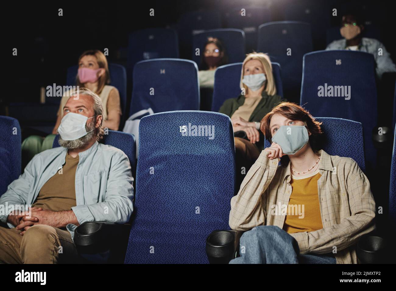 Grupo de hombres y mujeres usando máscaras protectoras viendo una película en el cine durante la cuarentena Foto de stock
