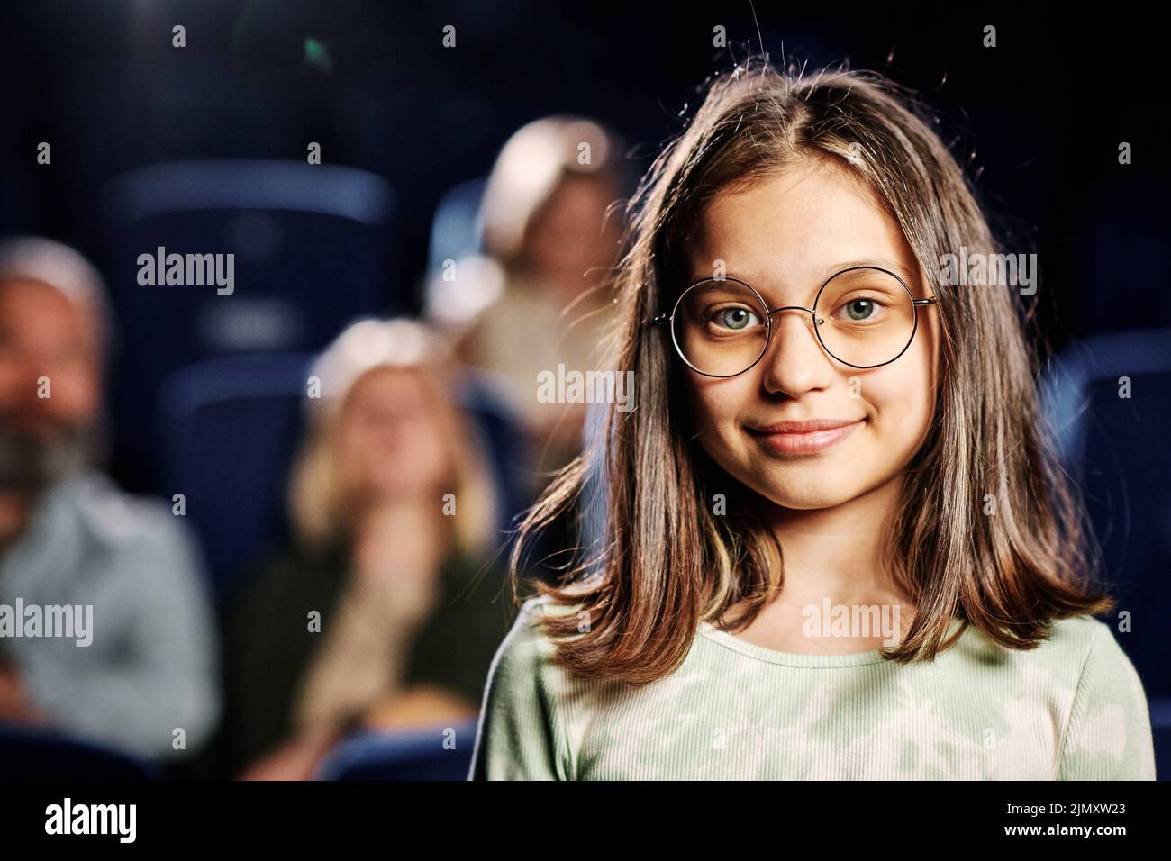Retrato de una niña caucásica preadolescente que llevaba gafas de pie contra los asientos en el cine mirando la cámara Foto de stock