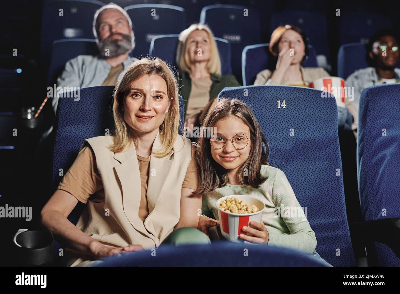 Retrato de una moderna mujer caucásica y su hija preadolescente sentada en el cine mirando la cámara Foto de stock