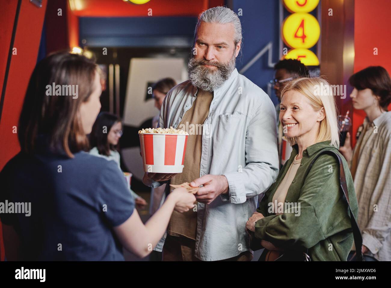 Una pareja adulta moderna que pasa sus entradas para la película a una joven trabajadora del cine Foto de stock