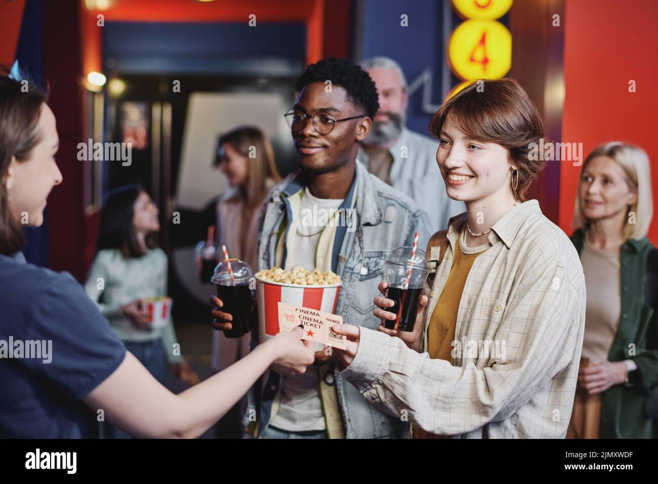 Alegre joven negro y mujer caucásica pasando sus entradas para la película a un trabajador de sala de cine Foto de stock