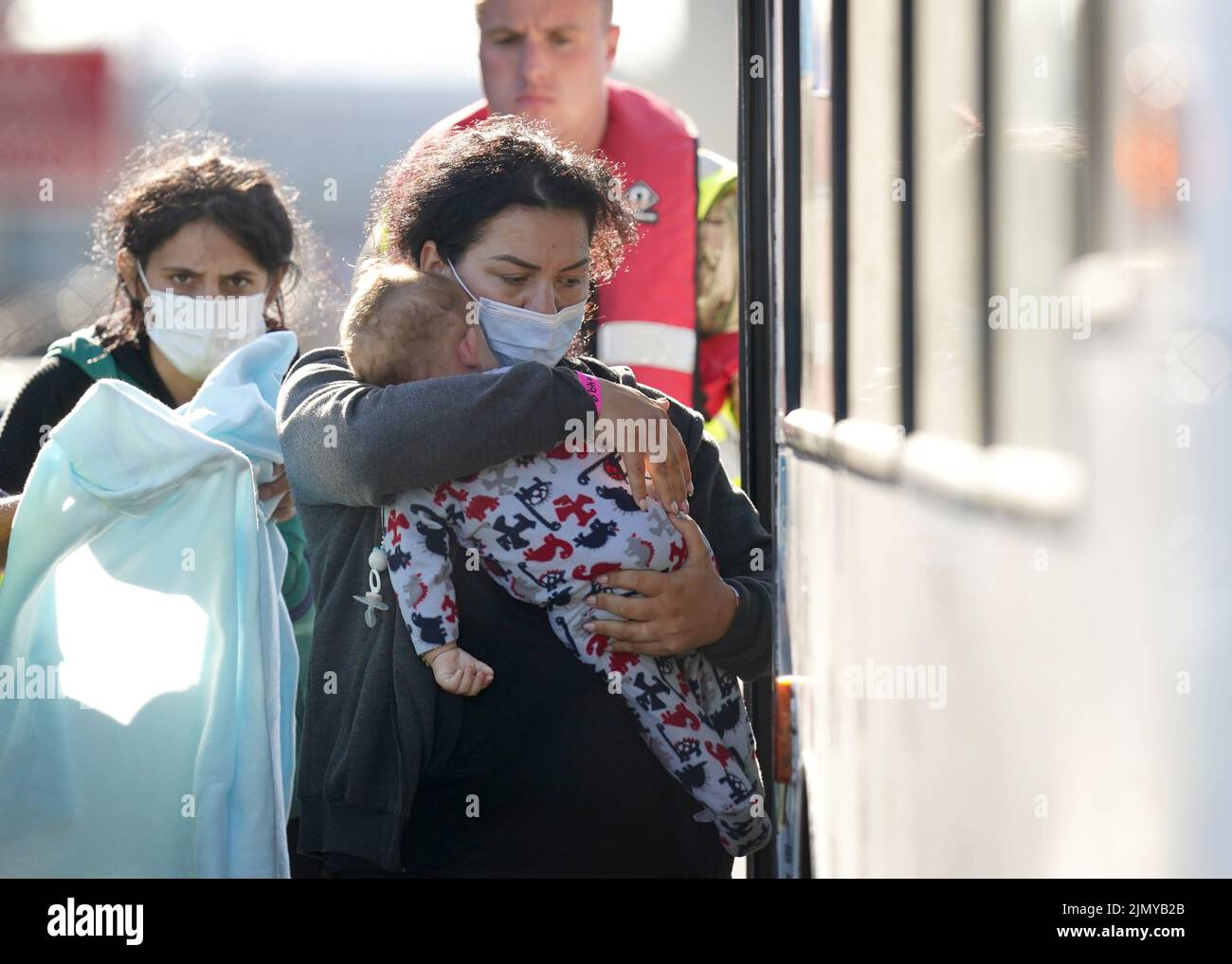 Una señora lleva a un niño pequeño a un autobús mientras un grupo de personas que se cree que son inmigrantes llegan a Dover, Kent, después de un incidente de un pequeño barco en el Canal de la Mancha. Fecha de la foto: Lunes 8 de agosto de 2022. Foto de stock