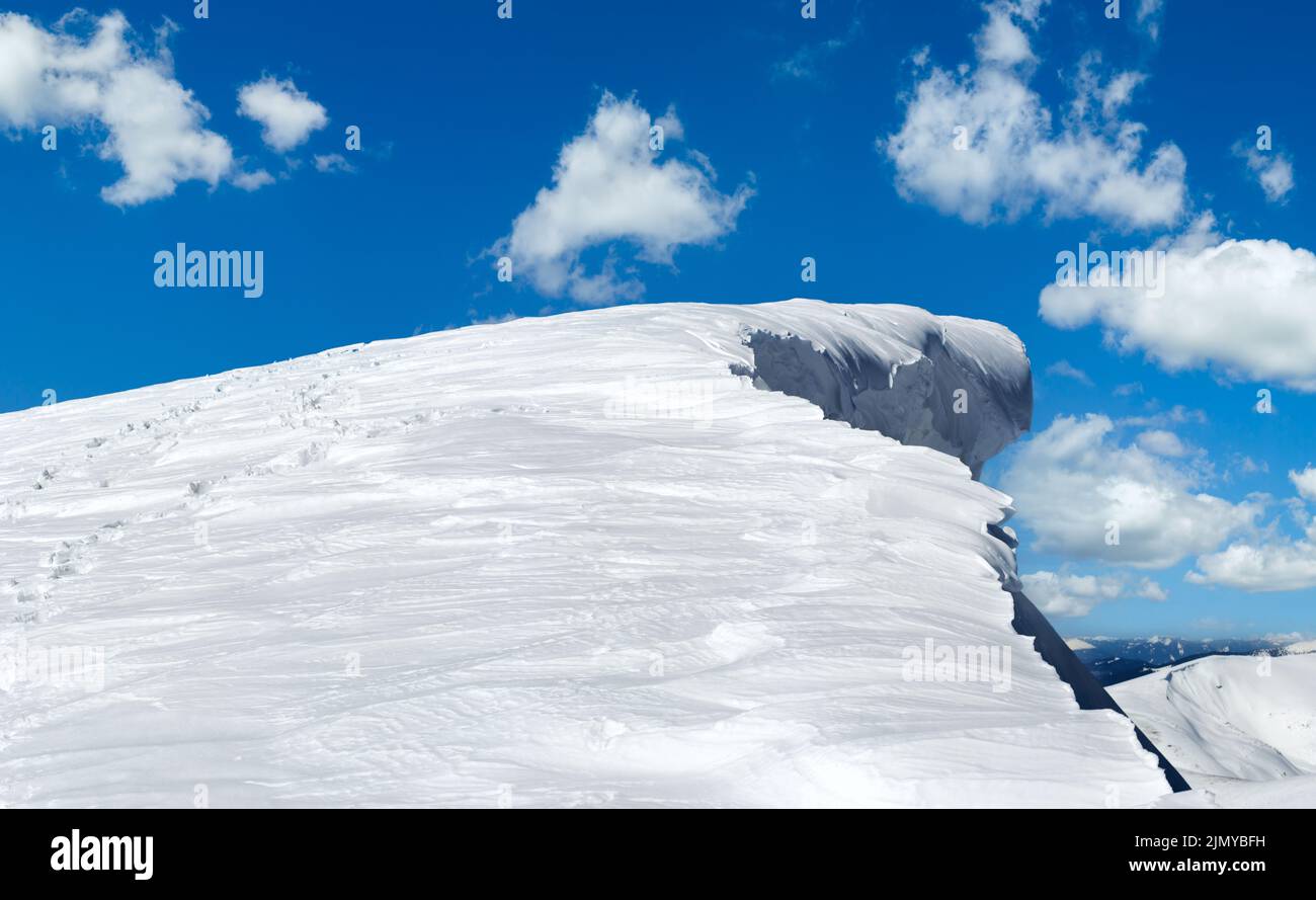 Cima de montaña de invierno con gorro de nieve de hada y huella humana en nevadas de seguimiento en las laderas de la montaña. Foto de stock