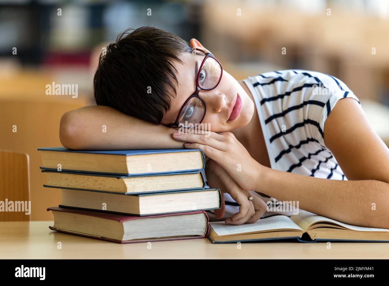 Mujer joven exhausta estudiando y preparándose para el examen en la biblioteca de la universidad. Educación concepto de personas Foto de stock