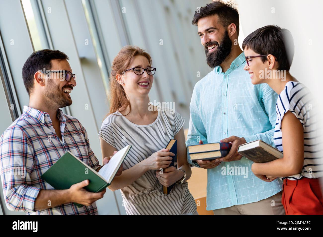Felices estudiantes universitarios estudiando con libros en la biblioteca. Grupo de personas multirraciales en la universidad Foto de stock