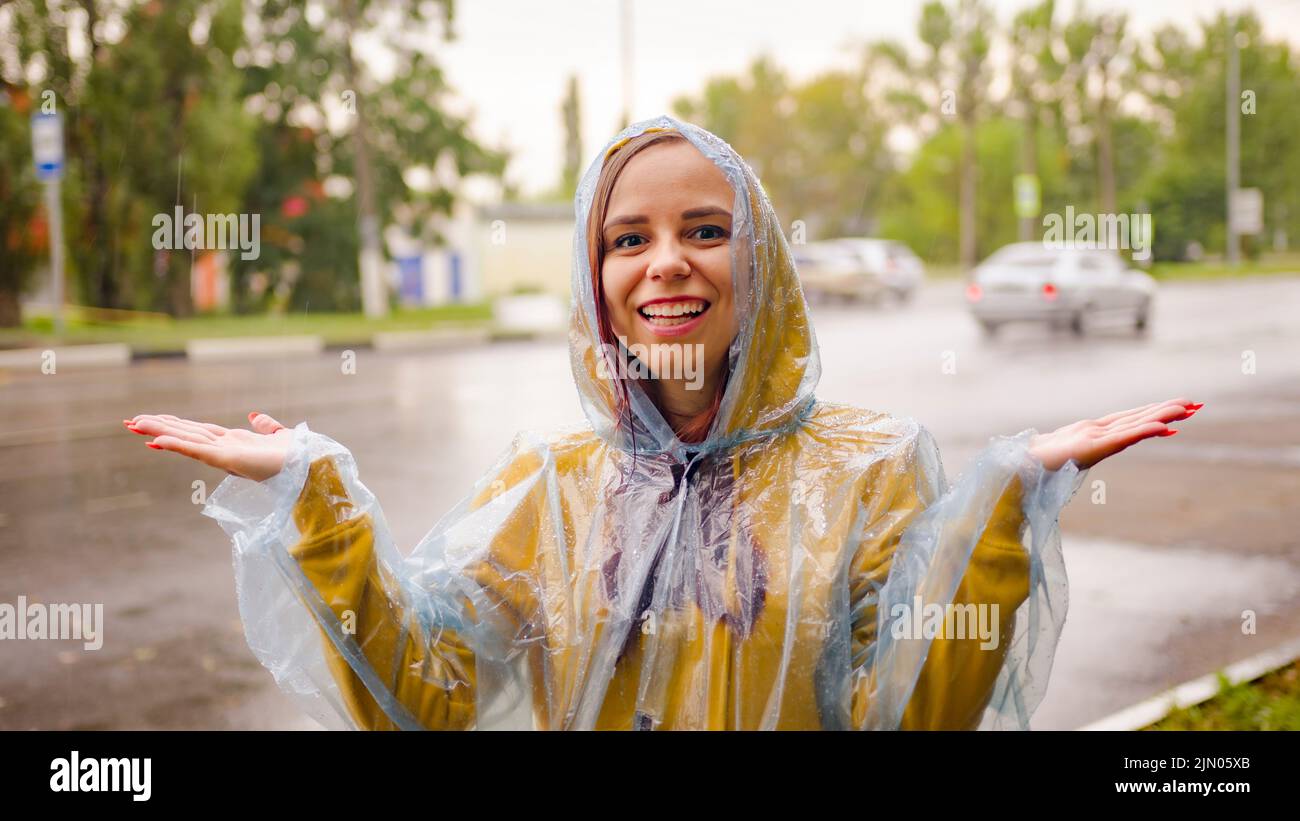 Mujer joven con chubasquero en la calle bajo la lluvia. Mujer positiva  atrapando gotas de lluvia con las manos, disfrutando del tiempo Fotografía  de stock - Alamy