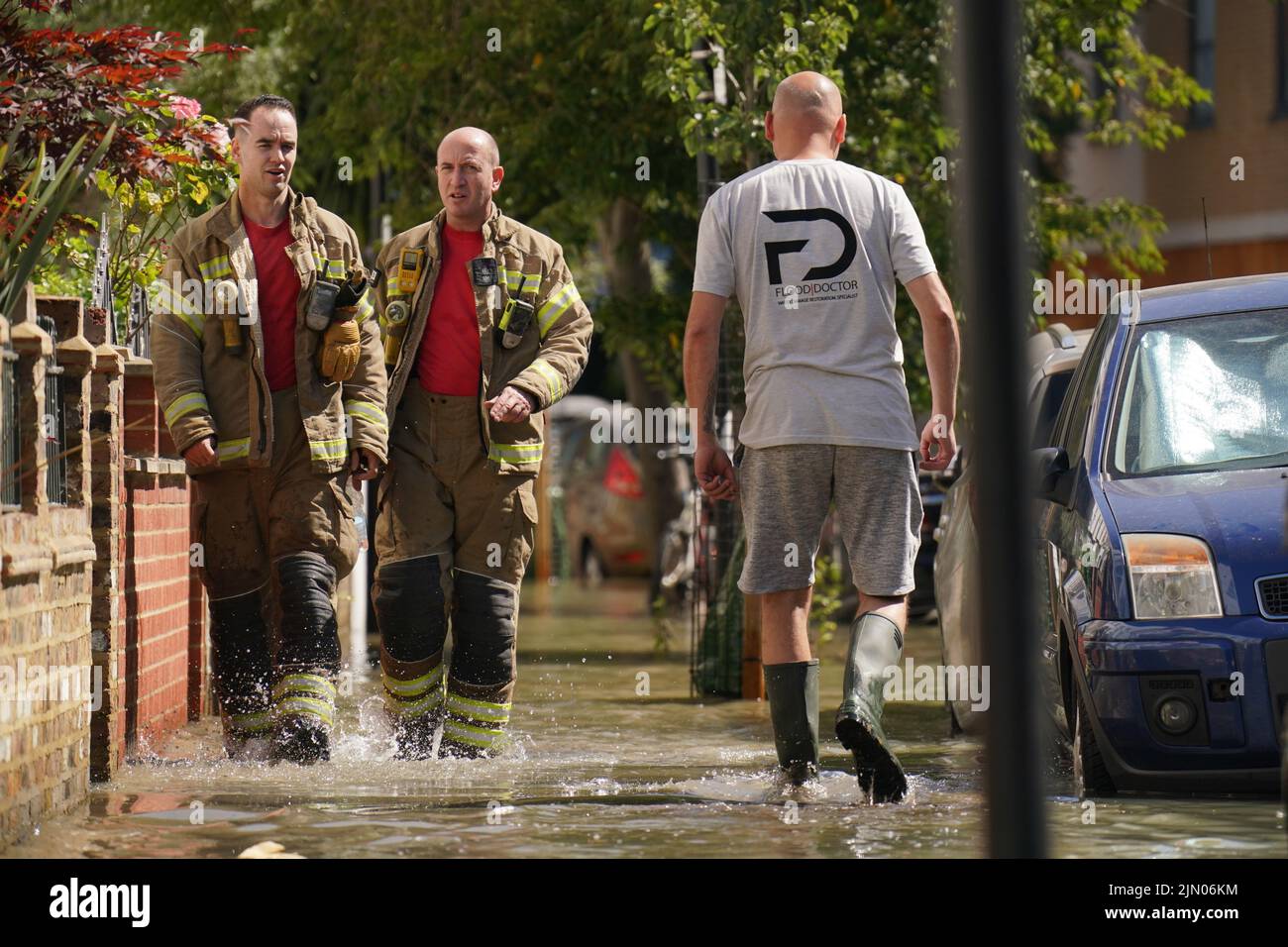 Los miembros de la Brigada de Bomberos de Londres pasan a un miembro del público mientras caminan en el agua de la inundación en Annette Road cerca de Tollington Road, Holloway, al norte de Londres, después de una explosión principal de agua de 36 pulgadas, causando inundaciones de hasta cuatro pies de profundidad. Fecha de la foto: Lunes 8 de agosto de 2022. Foto de stock