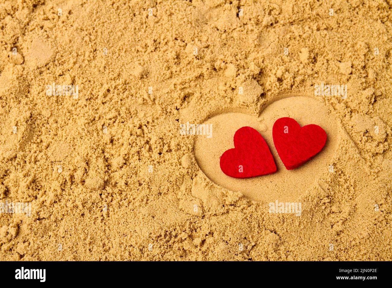 Dos corazones rojos en la arena de la playa. Concepto de vacaciones de luna de miel. Foto de stock